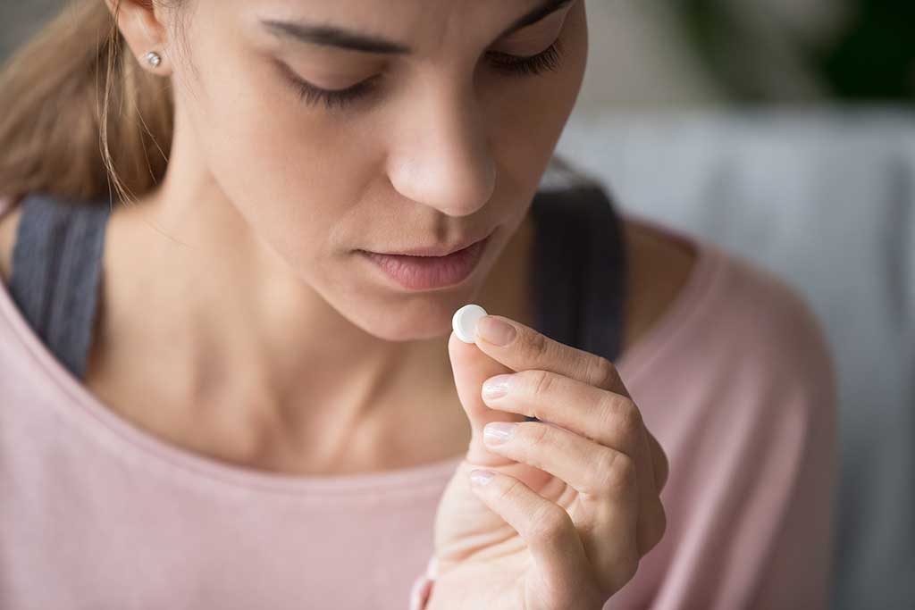 Close up of upset young woman holding pill