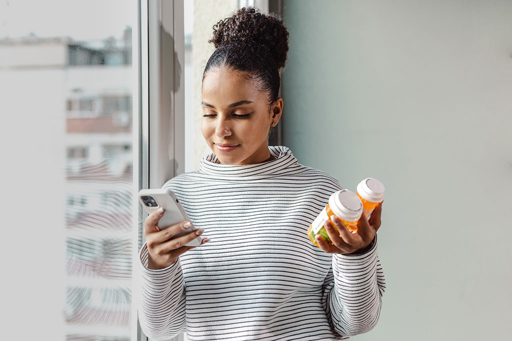 A young woman standing by the window and researching about the medicine online